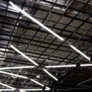 technicien remplaçant un tube néon par un tube LED dans un bâtiment professionnel